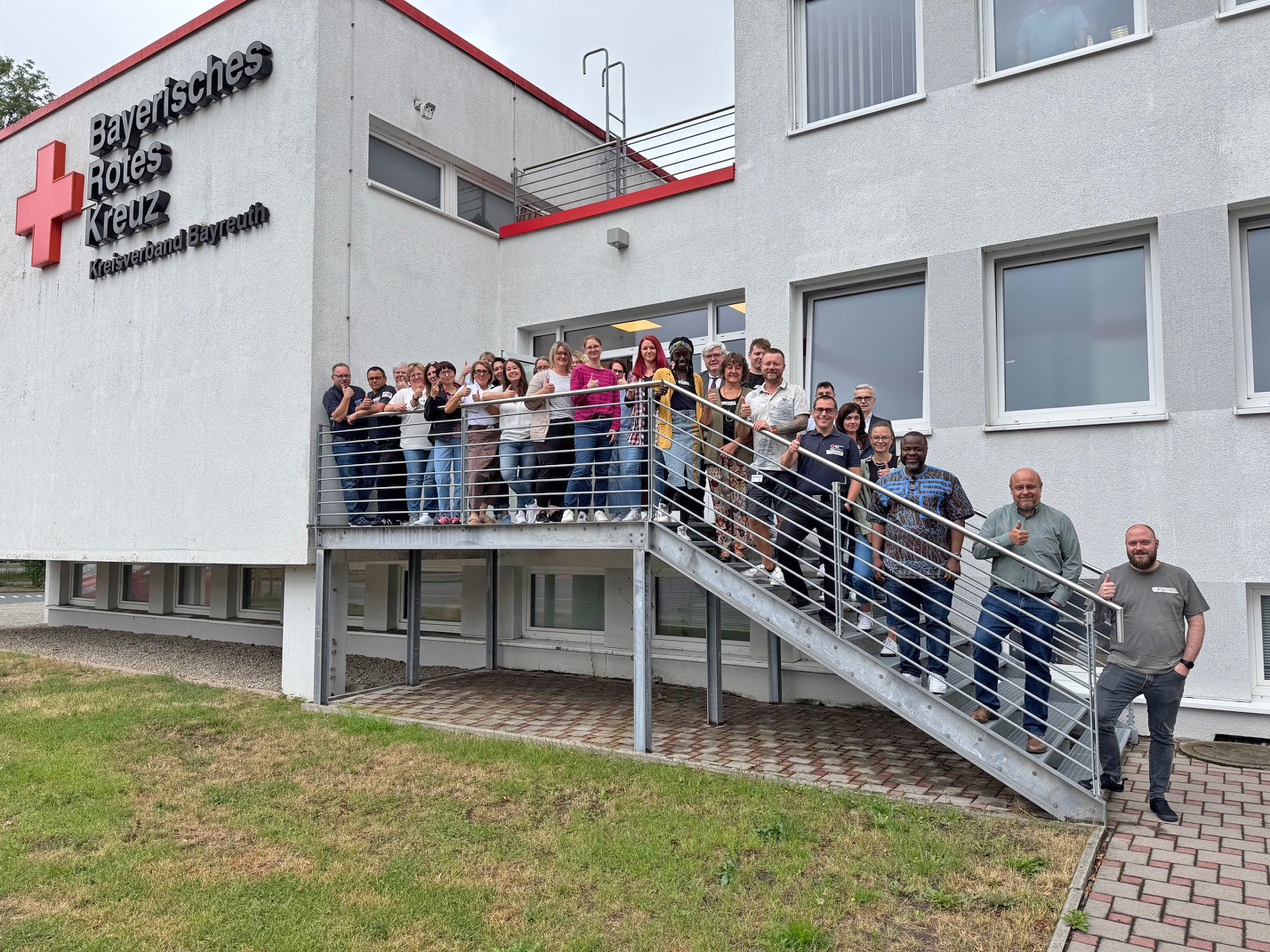 Teilnehmende der Schulung Internationale Fachkräfte: Chance und Herausforderung mit Dozentin Priscilla Hirschhausen und Ibukun Koussemou vor der Geschäftstelle des BRK Bayreuth. (Gruppenfoto)